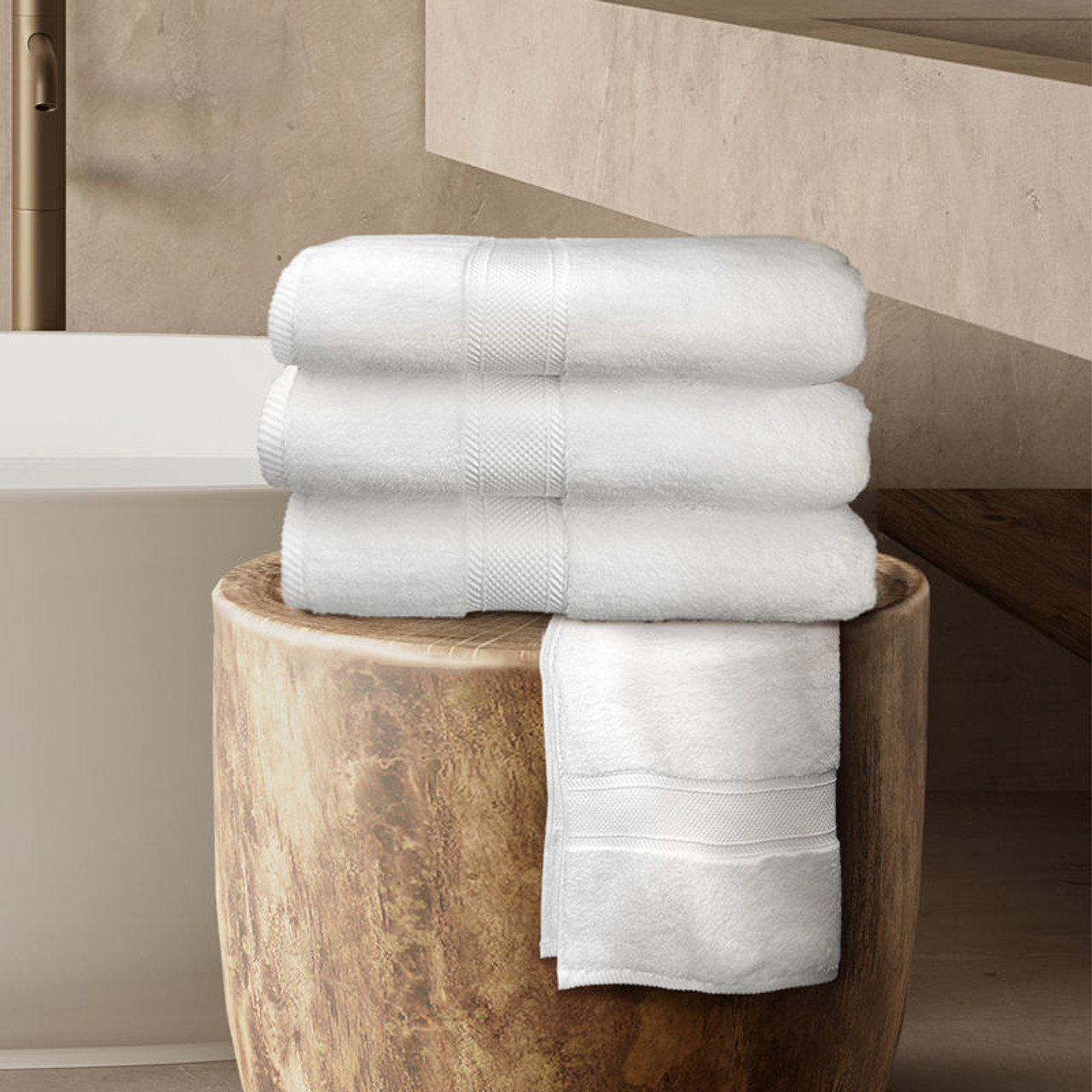 Three white bath mats neatly folded on top of a fourth mat, draped over a wooden stool